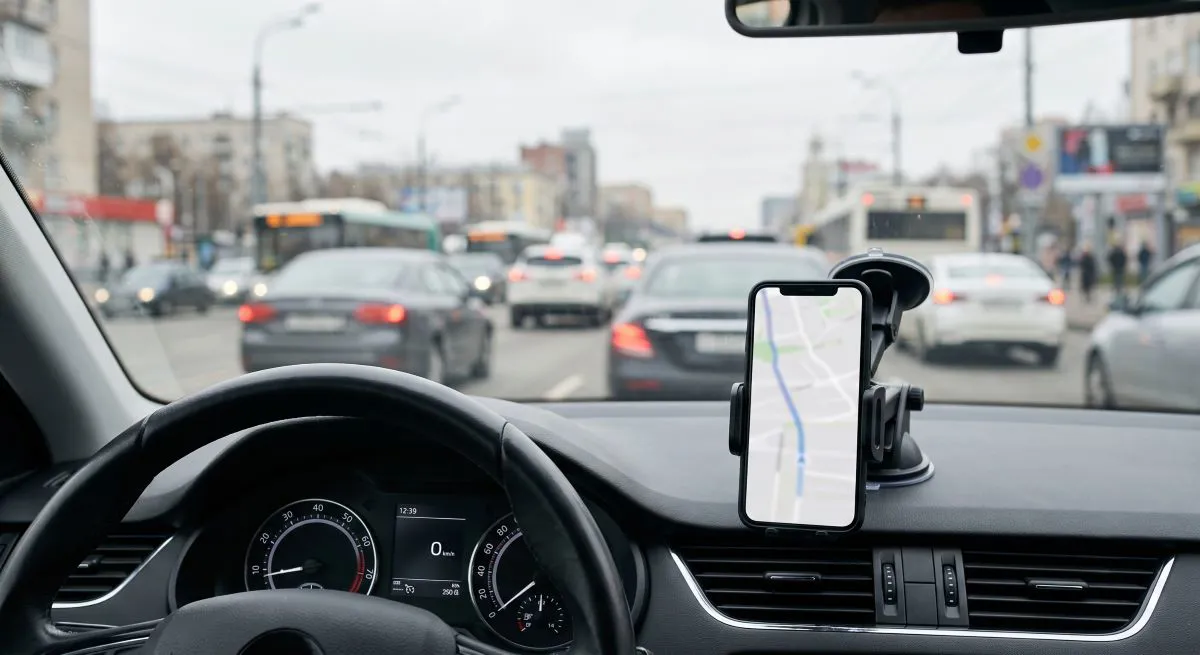 Araç içinde telefon tutucudaki açık navigasyon ekranı ve arka planda şehir trafiği