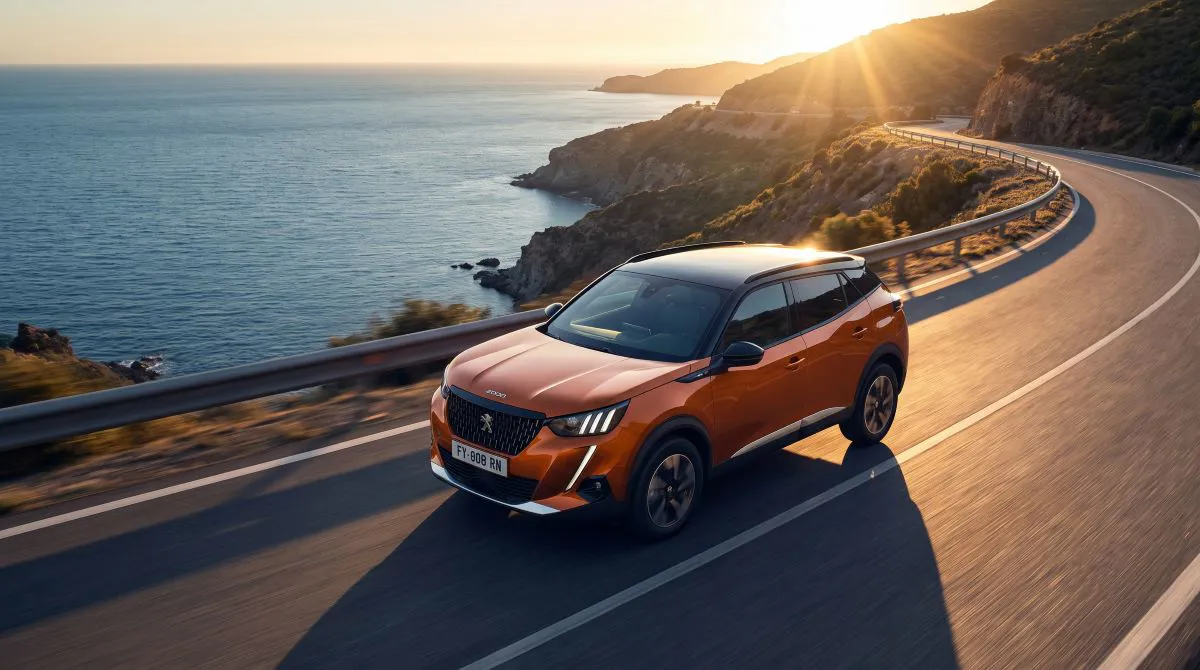 Mavi Peugeot 2008 kompakt SUV, deniz manzaralı sahil yolunda dinamik sürüş sırasında görüntüleniyor.